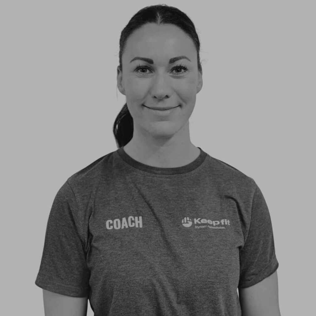 Ejer af Keep Fit, Natasja Keep står og smiler til kameraet iført en t shirt med Keep Fit logoet på det ene bryst og teksten coach på det andet