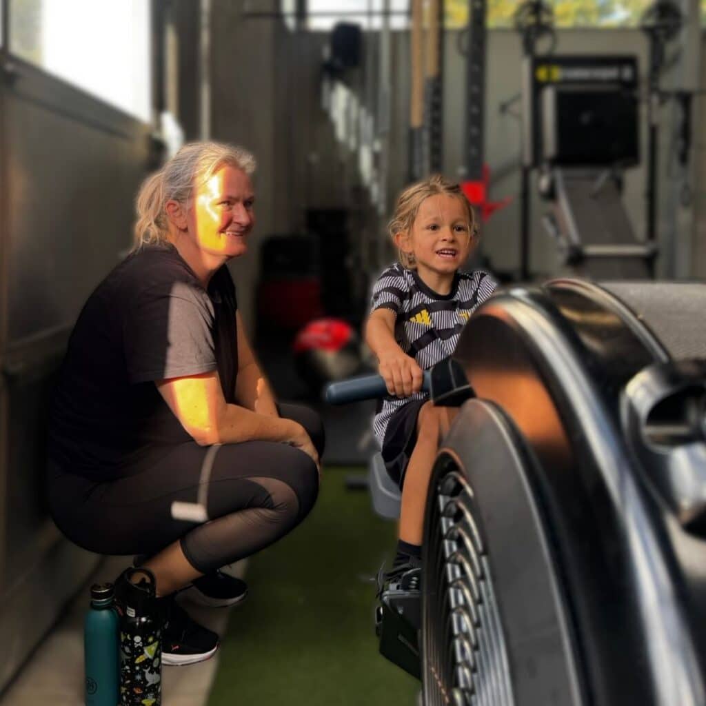 Voksen kvinder kigger på sit barn, der sidder på en ro maskine til FamilyFit i Keep Fit i Nørresundby